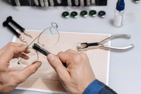 Young professional optical technician is fixing the bridge of eyeglasses in workshop with special pliers. Eyesight concept.